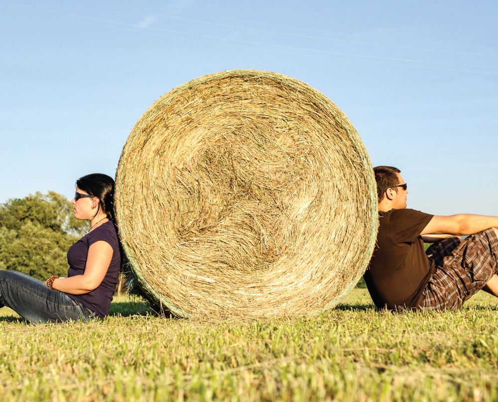 couple each leaning on opposite sides of a hay bale not speaking to each other